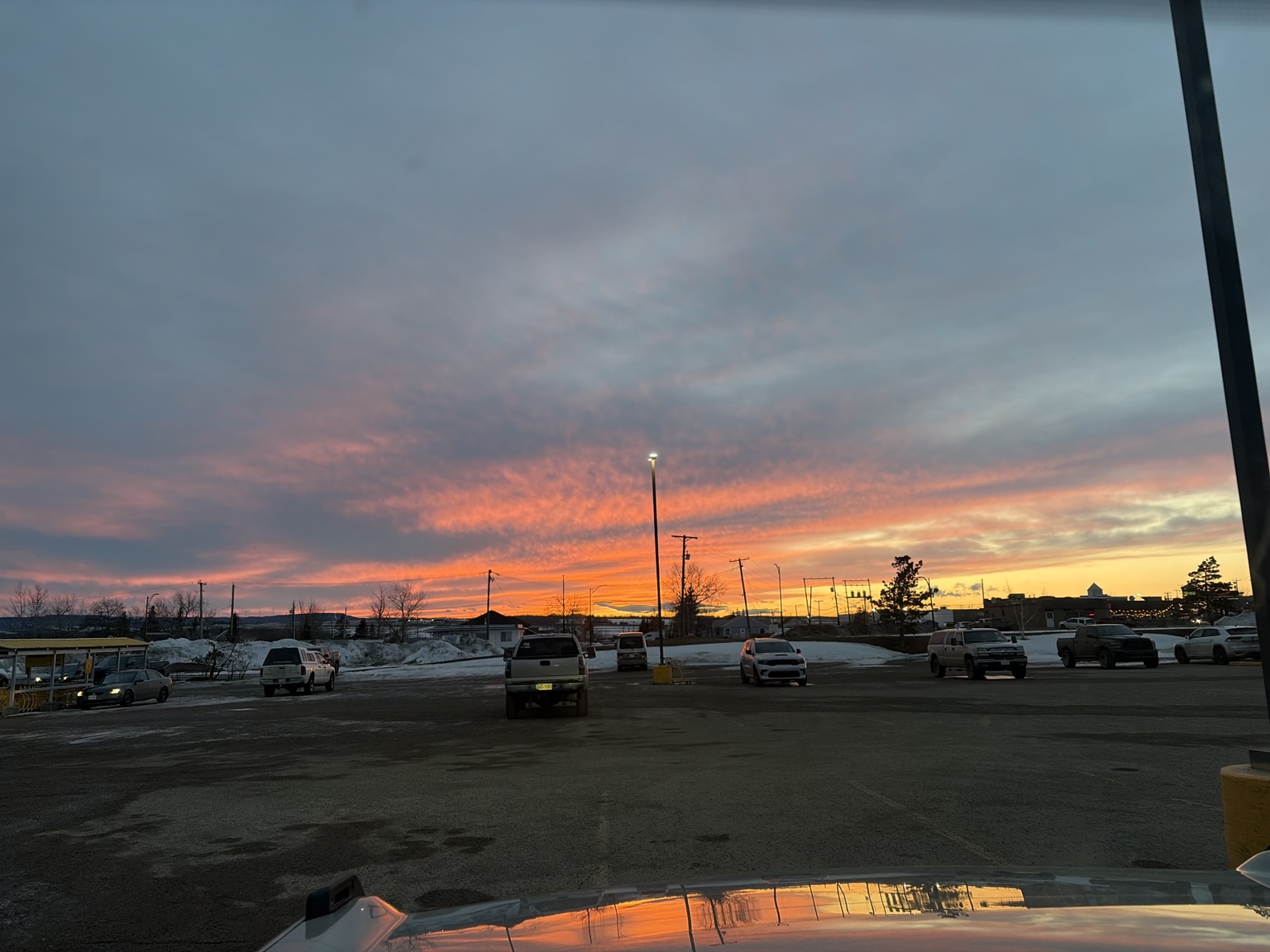 Orange sunset over a snowy parking area and vehicles